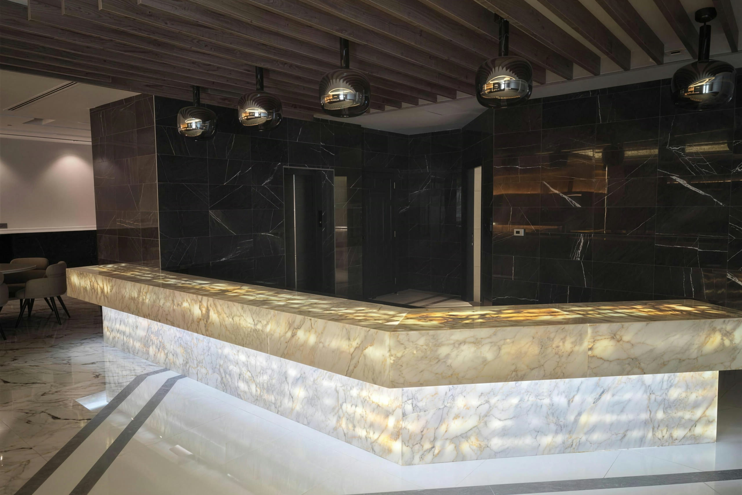 Backlit onyx bar with black marble wall and timber slat ceiling